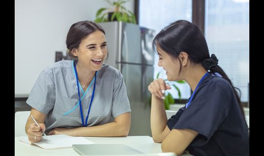 Two yoiung women in scrubs talk and laugh