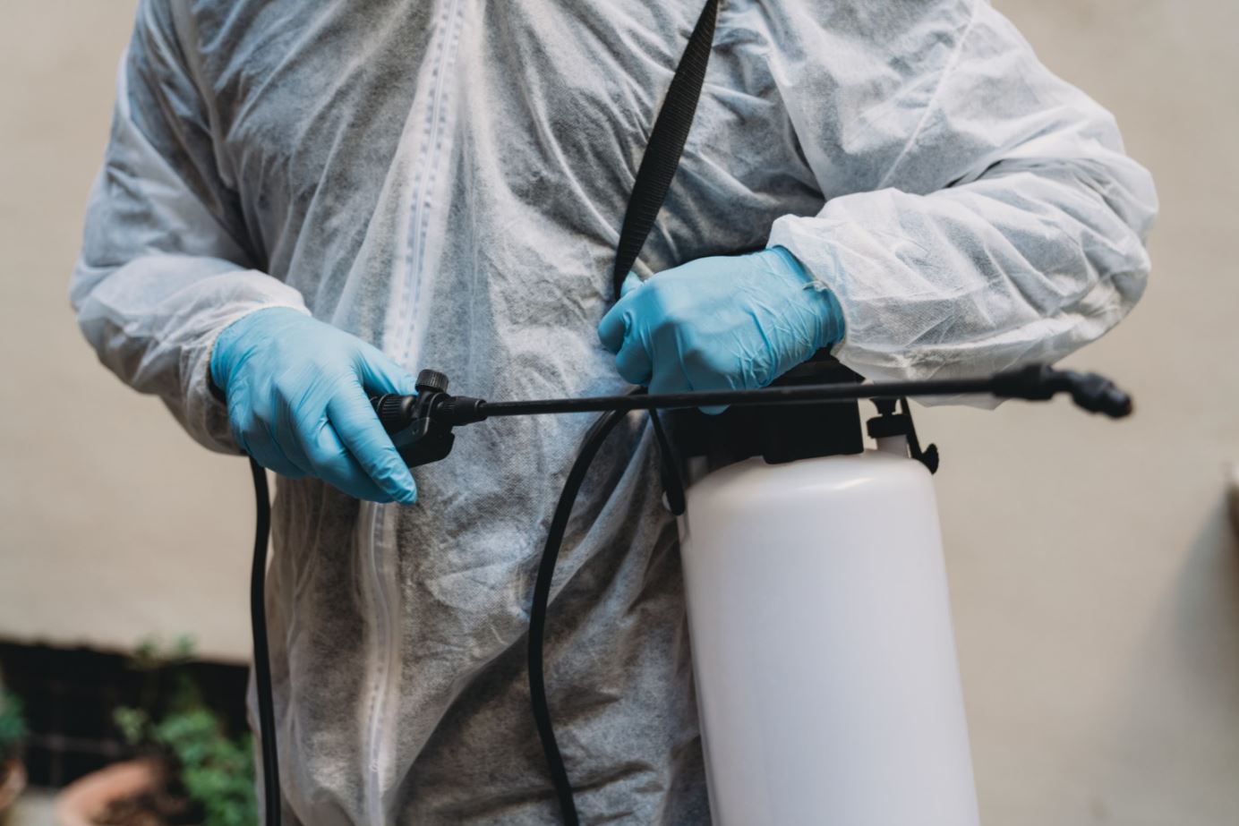 Person wearing coveralls and holding insecticide sprayer