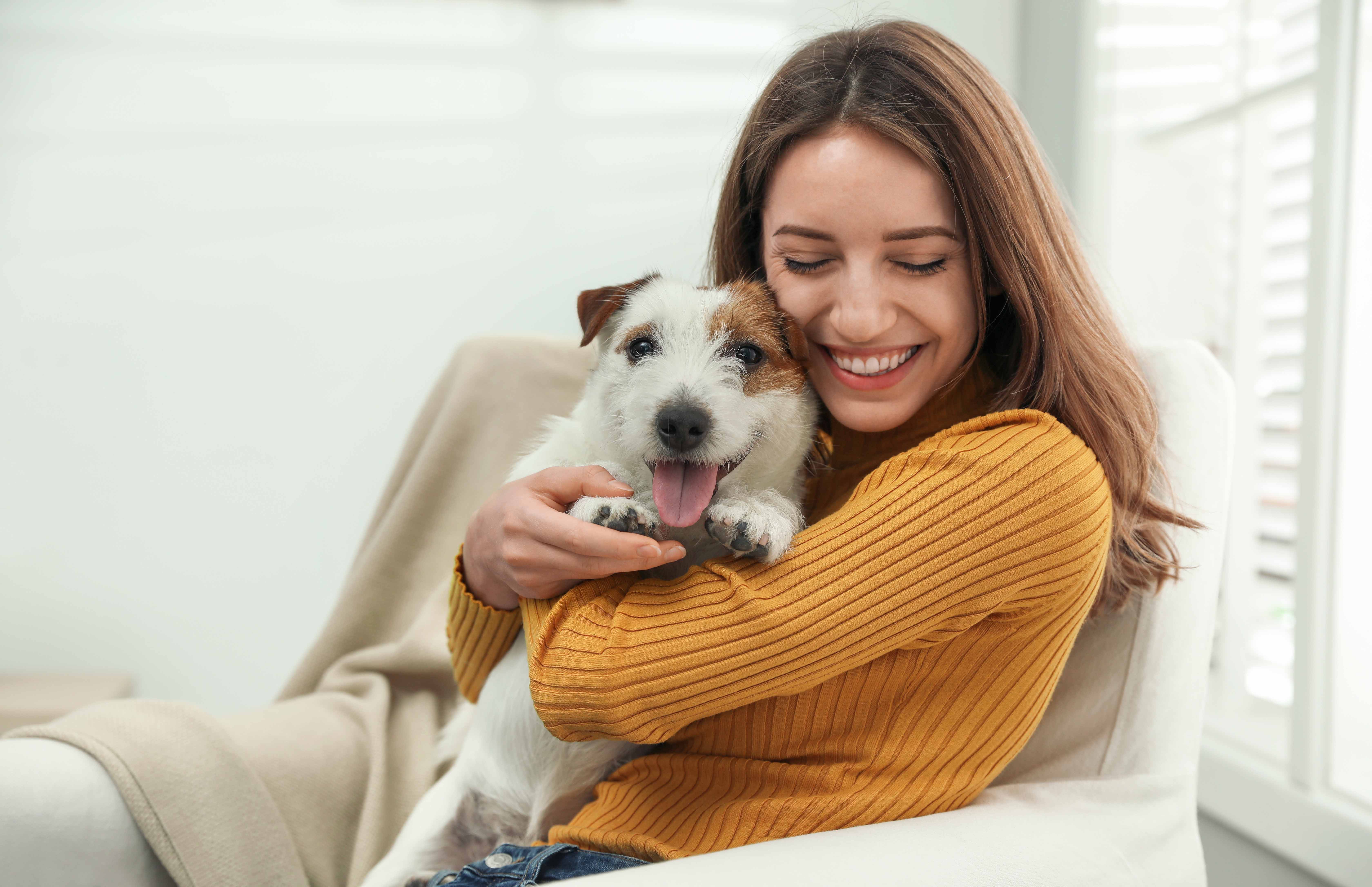woman in yellow sweater smiling while holding small dog